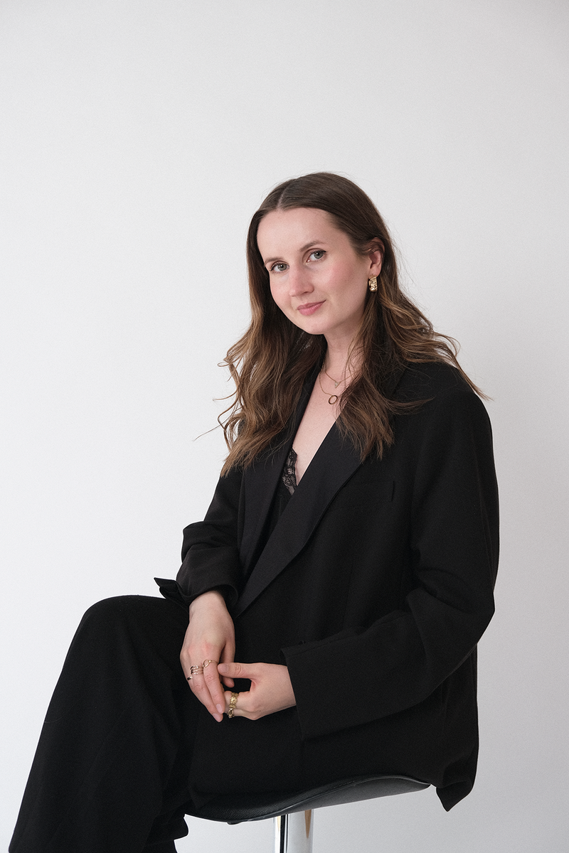 A portrait of Sofia: graphic designer, web designer and owner of ASCS Design. She's sitting down and looking into the camera, wearing a black suit. 