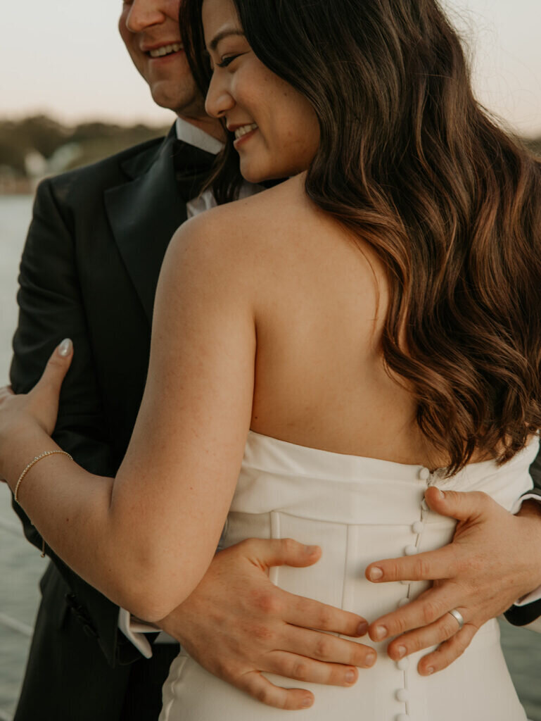 Groom holding bride by waist smiling.