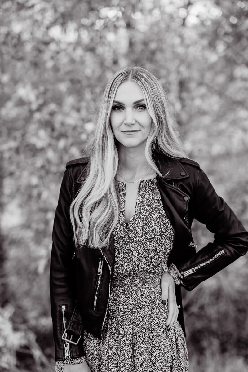 blonde woman in floral dress and black leather jacket subtly smiling at the camera
