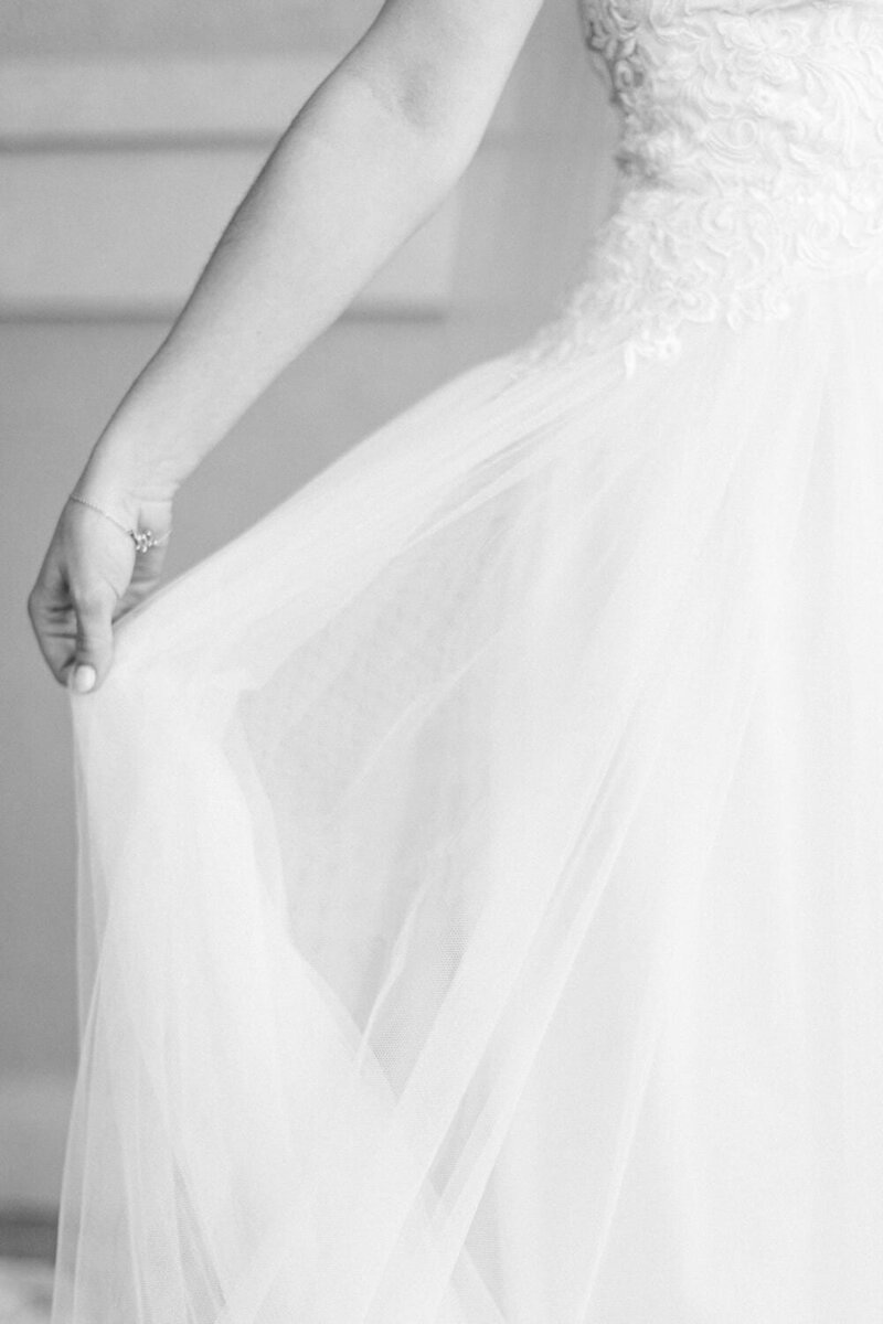 Capture the elegance of a bride getting ready, adjusting her dress in a stunning black and white photograph. A timeless and intimate moment preserved from her special day.