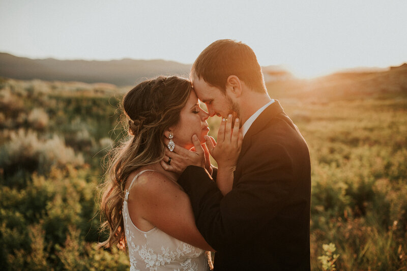 A bride and groom cup their hands around each others' faces as they touch noses