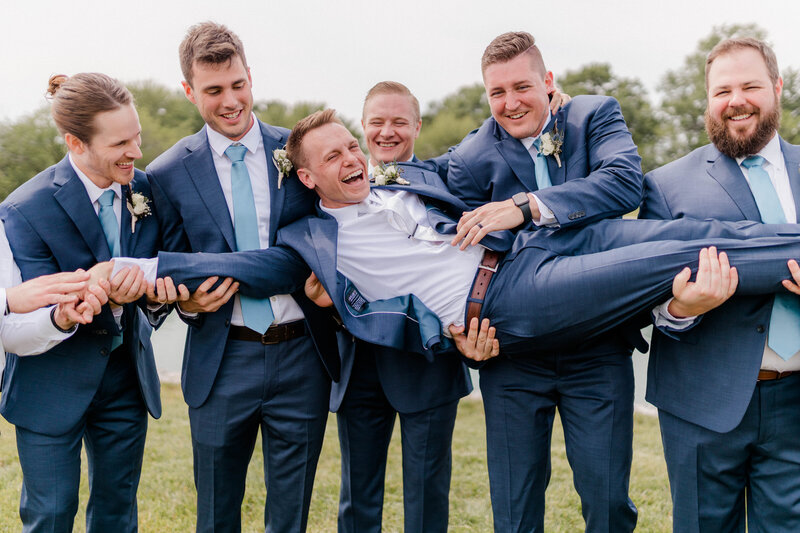 Groom is lifted up by all his groomsmen as they smile at each other for the camera.