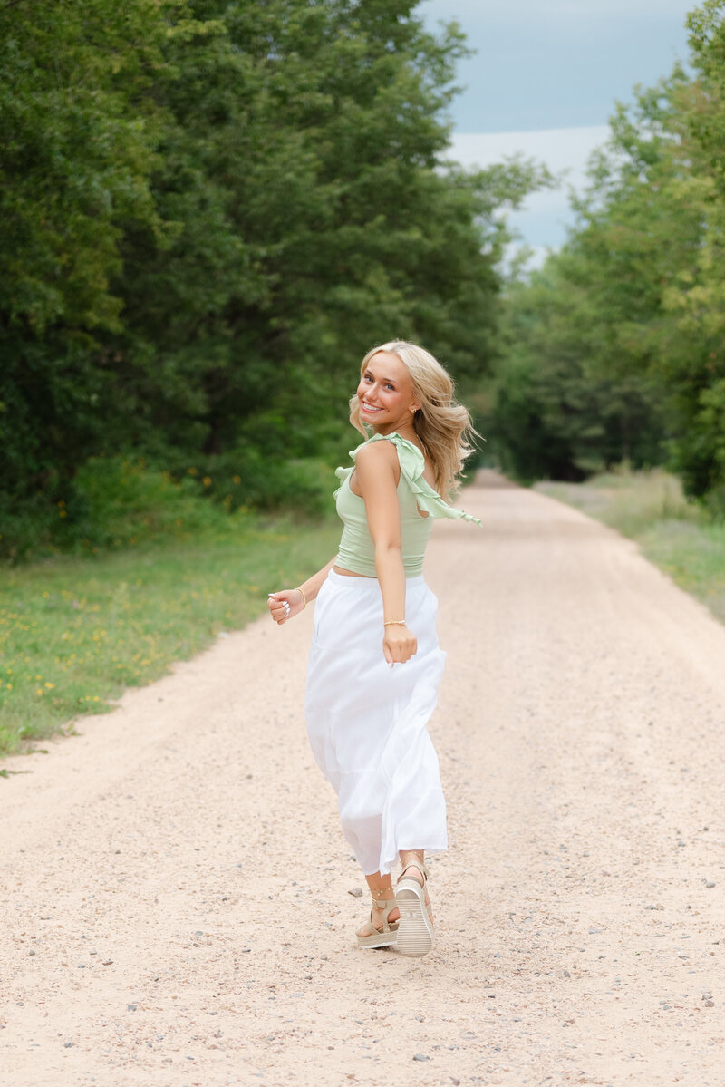 Blonde senior girl smiling and running away from the camera.