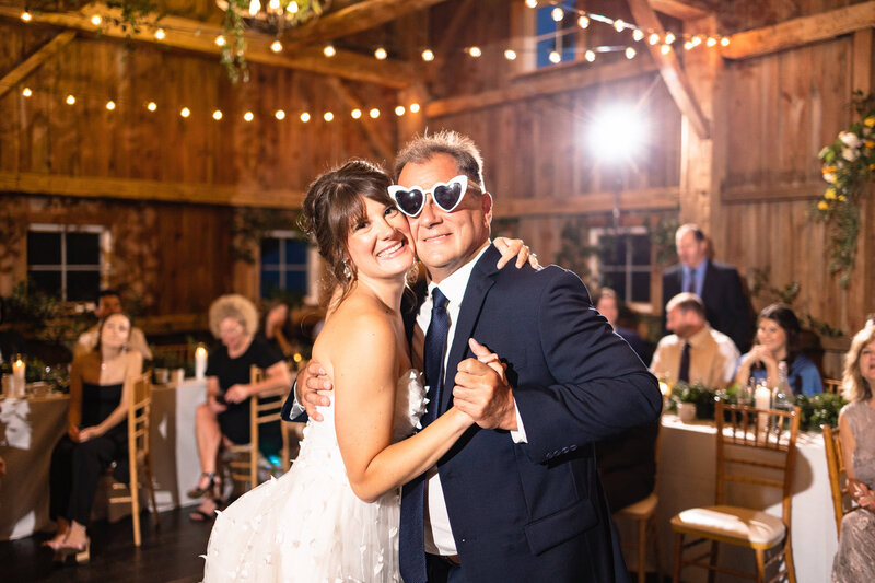 a bride hugging her father during their first dance as her dad wears heart shaped glasses