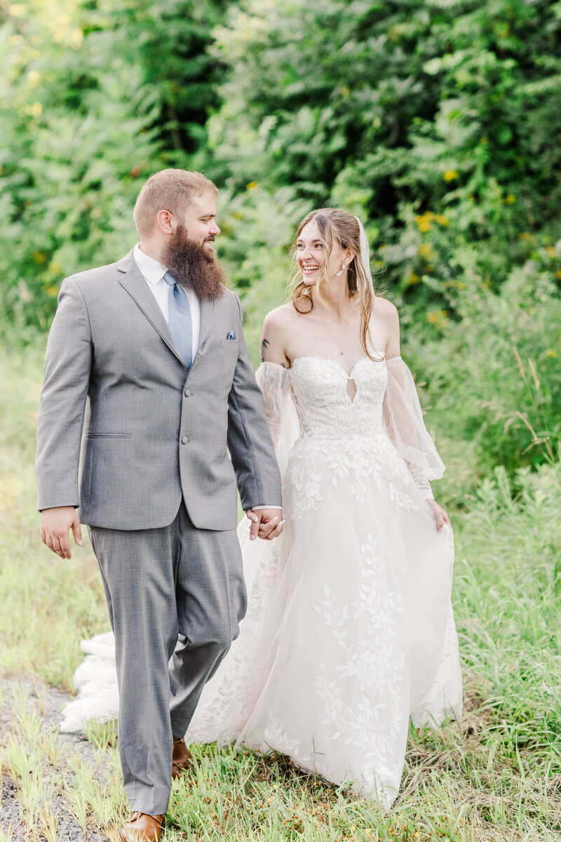 bride and groom walking hand in hand next to tall greenery during wedding photo session in upstate ny