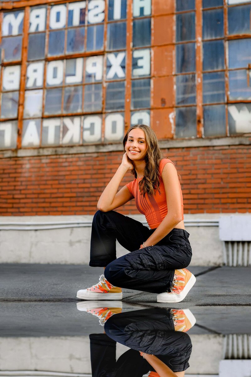charlotte senior bends down wearing black pants and orange top with decorative sneakers
