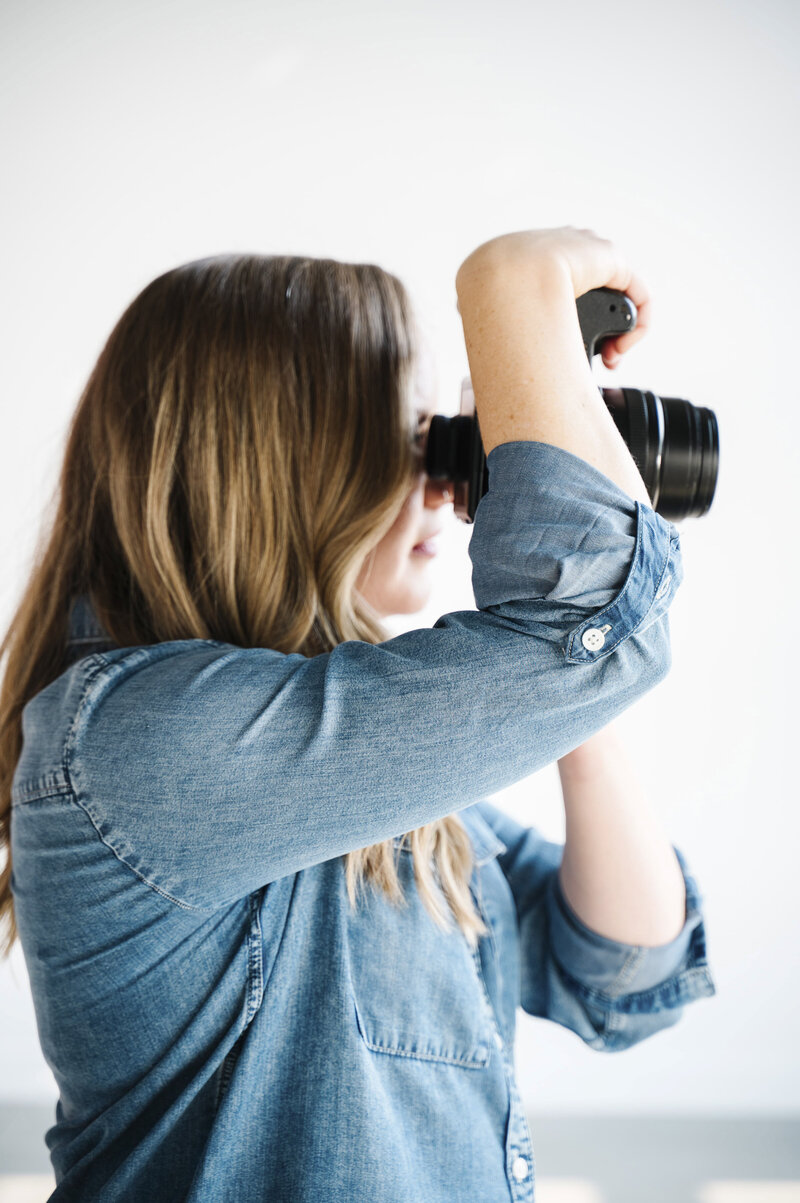 A side angle photo of Krista Marie, facing away from the camera and holding her camera up to her eye, while taking brand photos