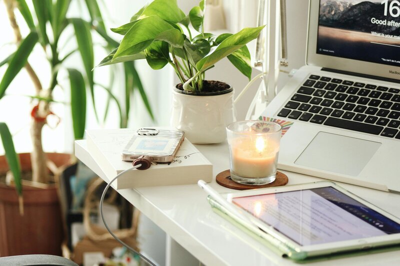 Lit candle on desk with plant and keyboard. 
