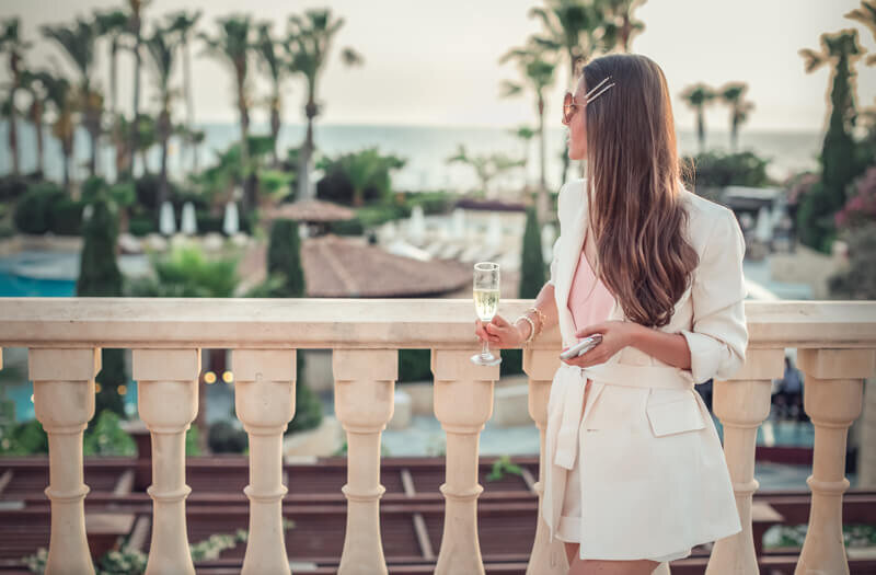 Business woman standing on luxury resort balcony holding a cell phone and glass of champagne