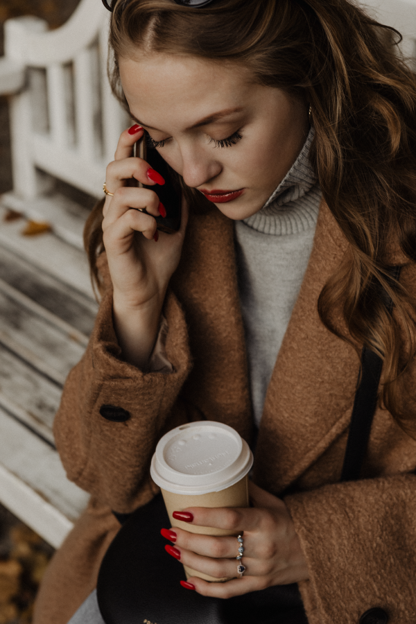 Young woman in brown coat on the phone holding cup of coffee | Brand By Design