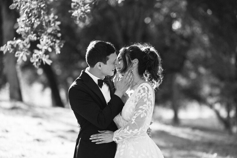 black and white photo of couple kissing while groom caresses bride face. Black tie suite and while long sleeve dress 