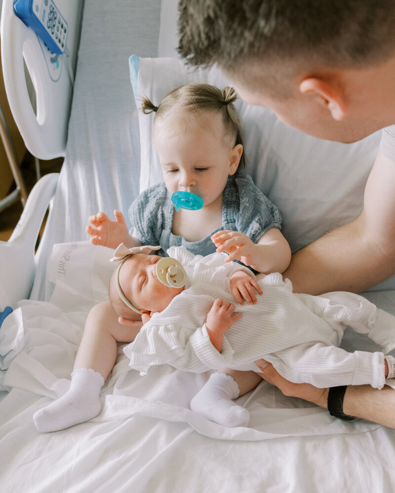 sibling holding newborn on hospital bed