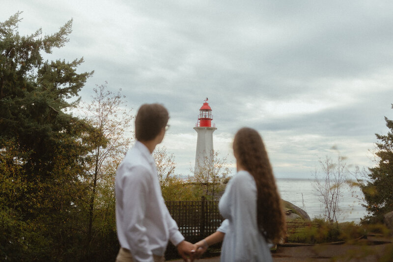 young couple holding hands and looking off in the distance to a lighthouse
