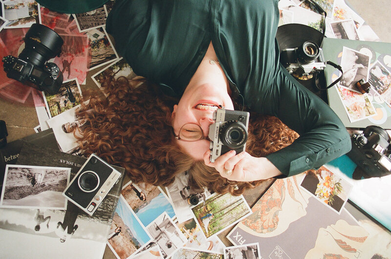 Film photo of Allison Bolin Texas wedding photographer laying on the ground with a camera surrounded by cameras and printed photos