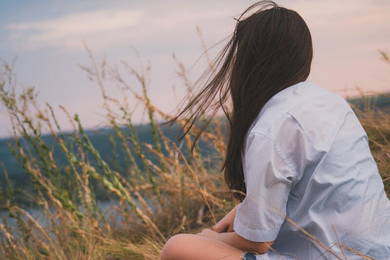 Woman sitting in a grassy field with her back turned, symbolizing emotional stillness and personal transformation through EMDR