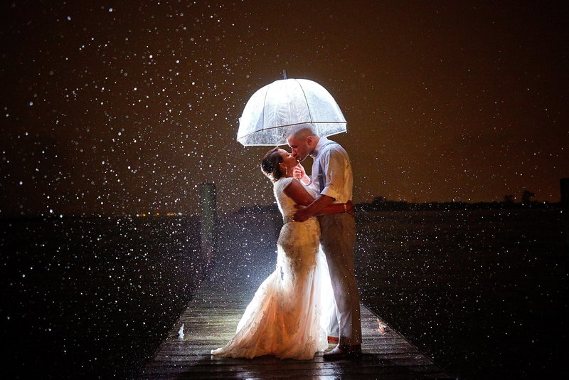 Embracing bride and groom on a dock in the rain