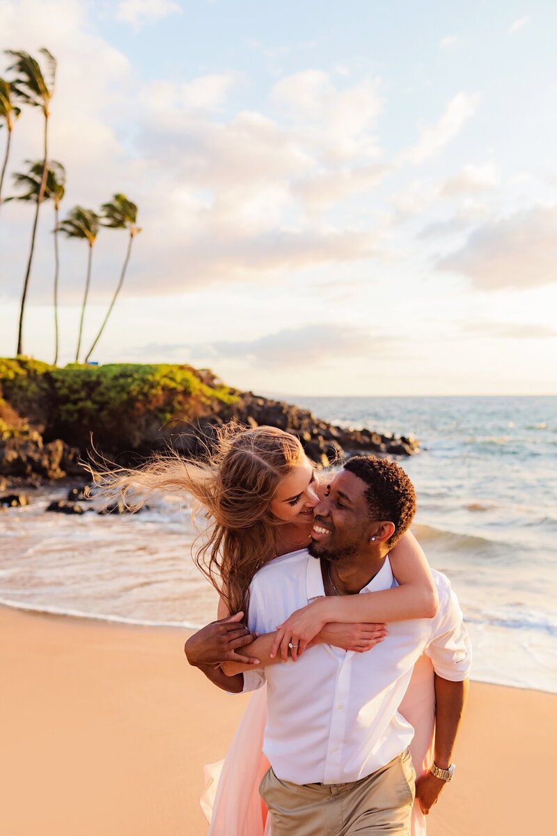 Man piggybacks his girlfriend as she leans in for a kiss during their couples photo session in Maui