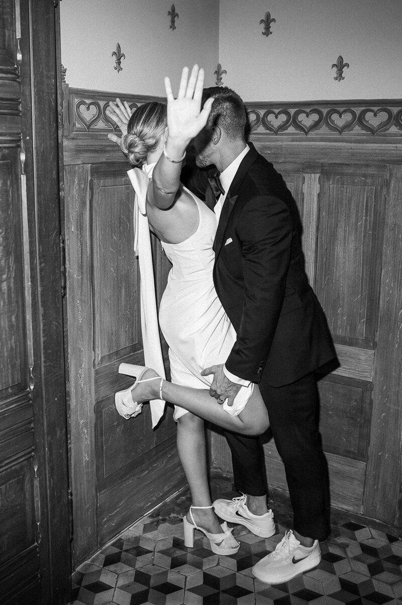 a bride and groom kiss in a corner, the bride is holding up her hands in a fun way