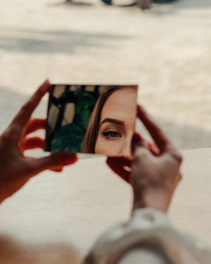 Woman holding a mirror and gazing into it thoughtfully, representing personal reflection and trauma healing through somatic psychotherapy in Manhattan.