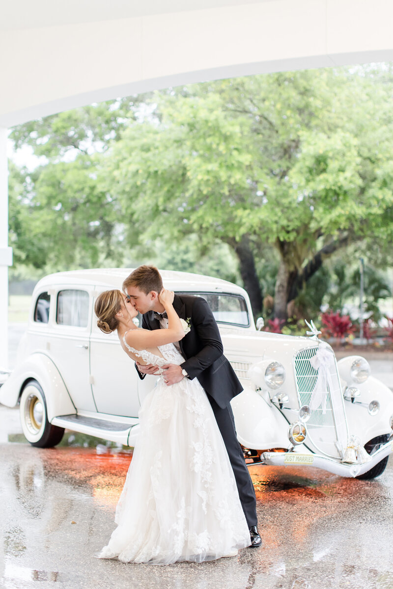 bride and groom kissing in front of a classic car