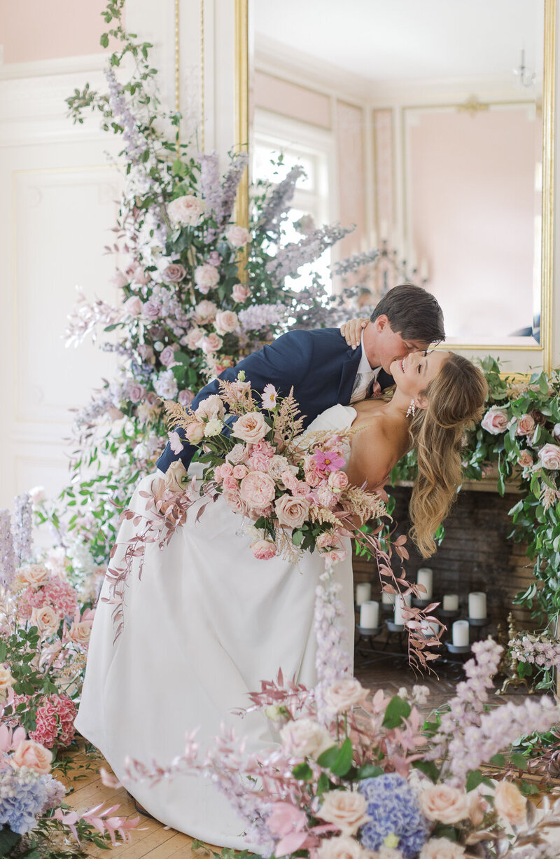 Couple kisses with flowers surrounding them on wedding day