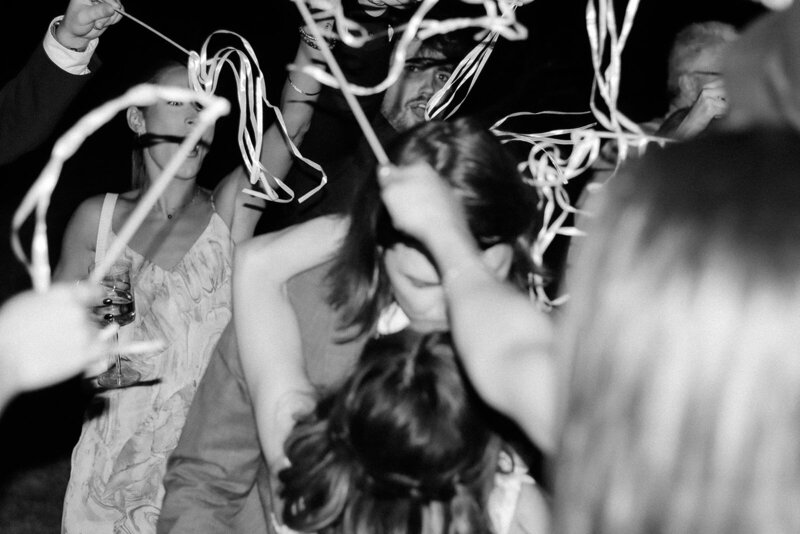Groom dips bride and kisses her during getaway while streamers from guests surround them.