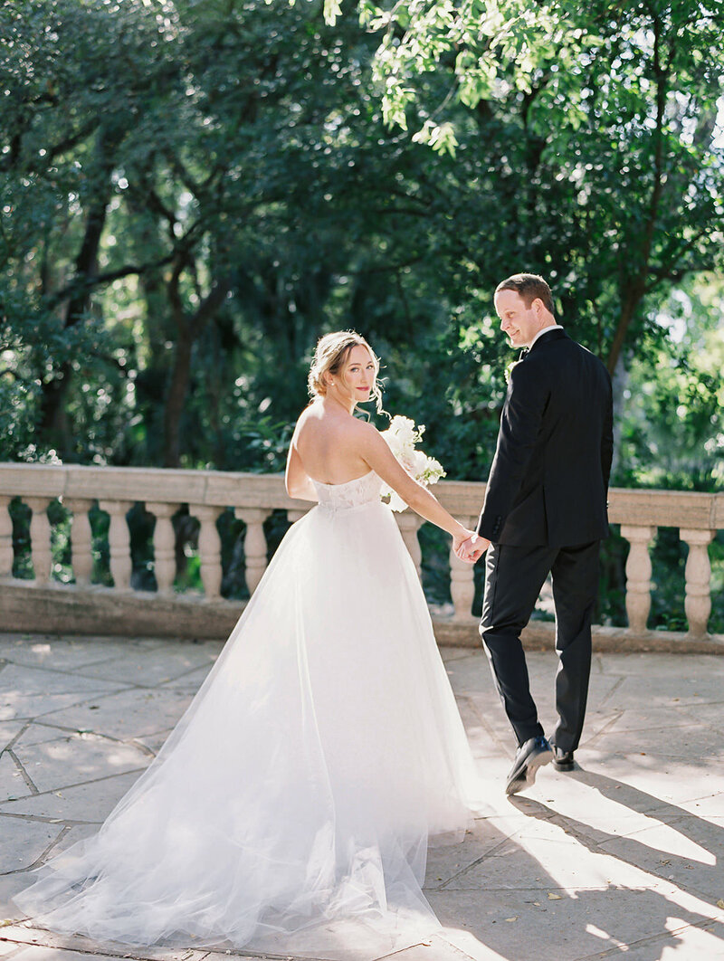 film image of a bride and groom walking away from the camera with the bride looking over her shoulder at Laguna Gloria