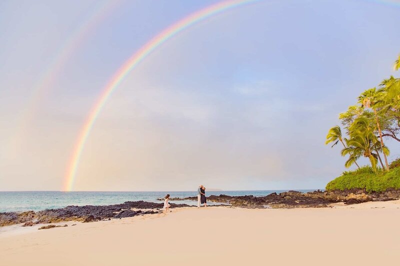 Family plays on the beach under a rainbow on a sunny day in Maui for family photos