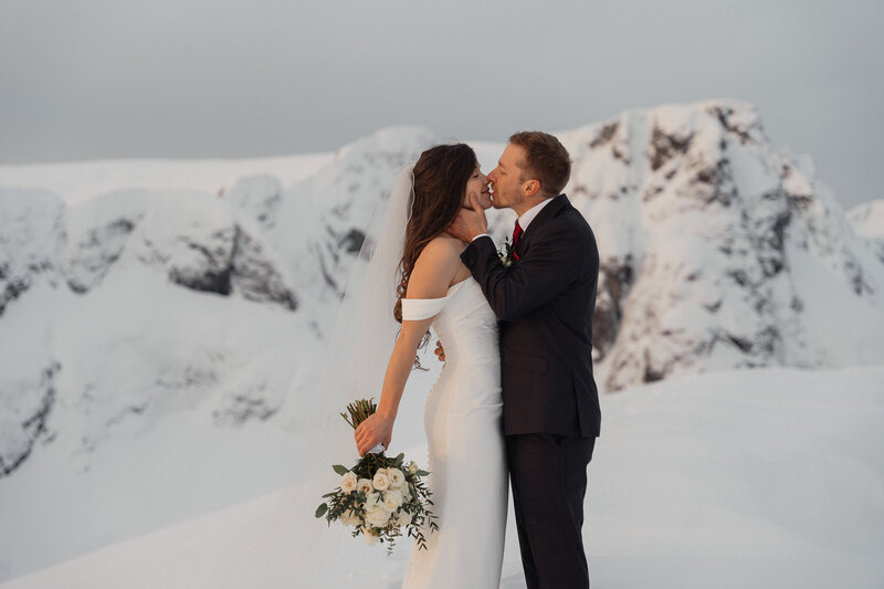 Bride and Groom kissing on top of a snowy mountain on Vancouver Island during their helicopter elopement