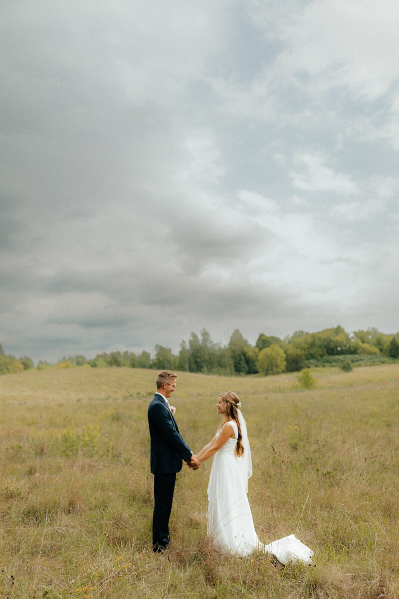 bride and groom in field holding hands