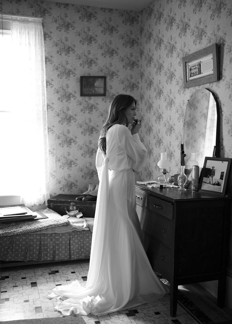 bride applying lipstick while looking in the mirror in her wedding gown