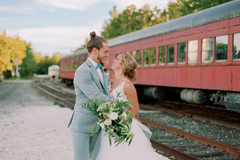 A couple leans in for a kiss with a red train behind them.