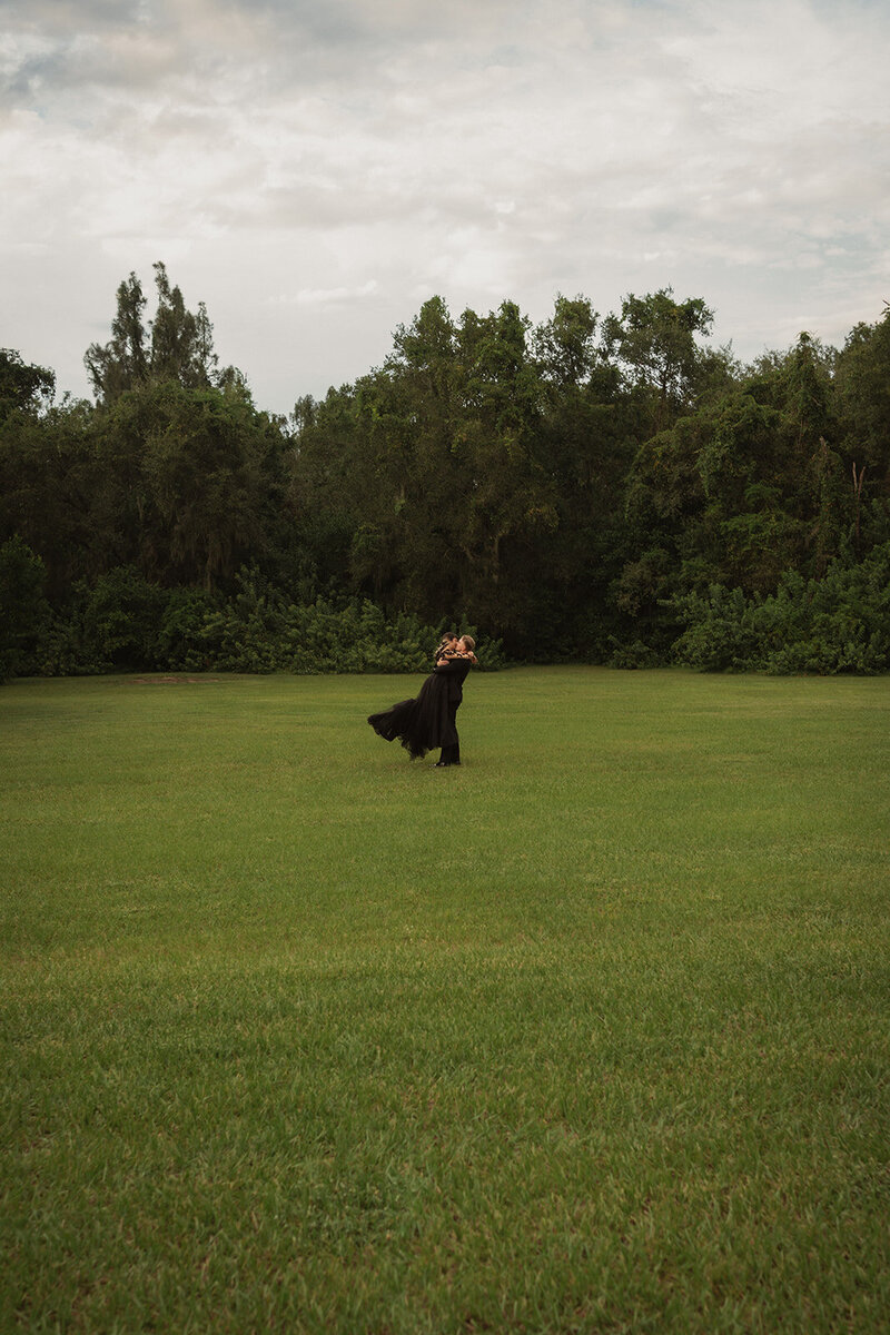 happy couple spinning around kissing outdoors on grass