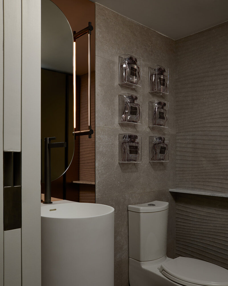 A before and after bathroom transformation of a simple bathroom design into a luxury bathroom featuring an elegant sink and toilet remodel, an oval vanity mirror, and textured grey walls