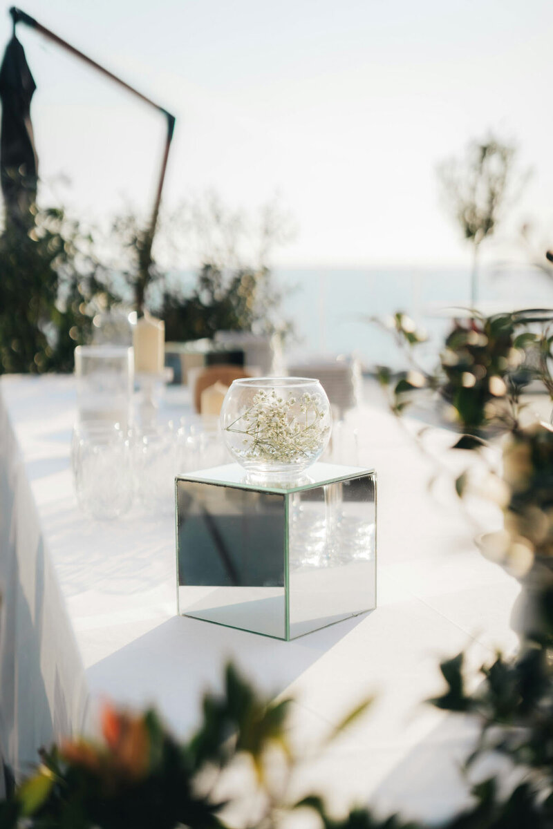 Minimalist outdoor table setup with mirror cube and sea view in background