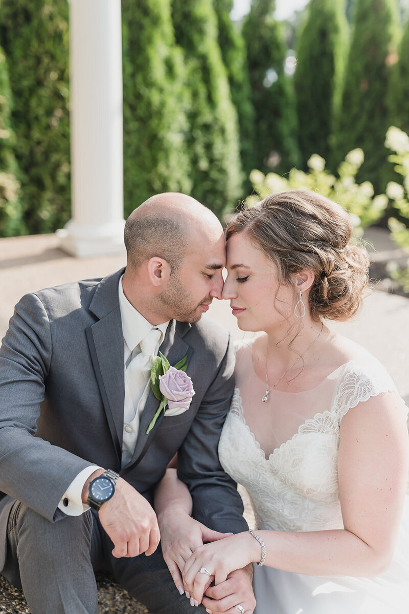 Bride gently holds groom’s face as they sit close, smiling with love and trust on their wedding day at Planterra Conservatory
