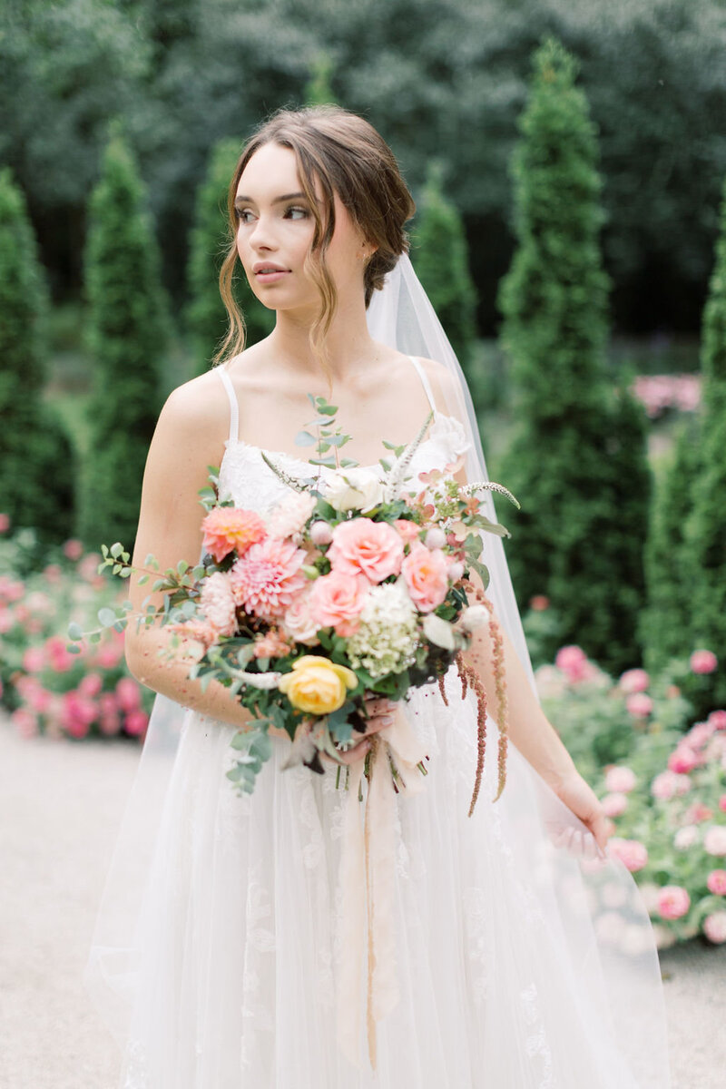 Bride with a low bun and soft tendrils looks in the distance at Newfields, Indianapolis Wedding Hair and Makeup