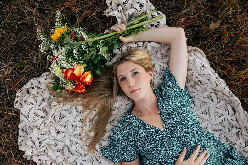Senior girl laying on blanket holding flowers while gazing at the camera. 