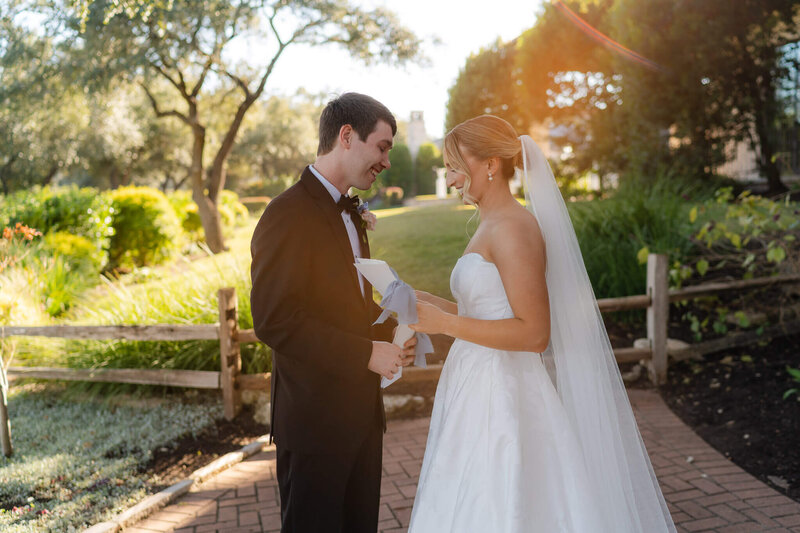 A husband and wife run across the lawn at their wedding venue happily as he holds her veil