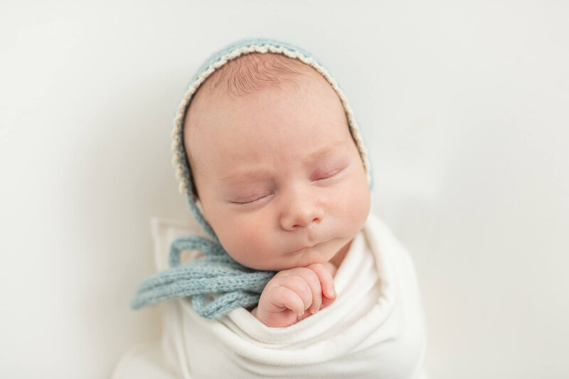 newborn baby boy in white and blue bonnet sleeping