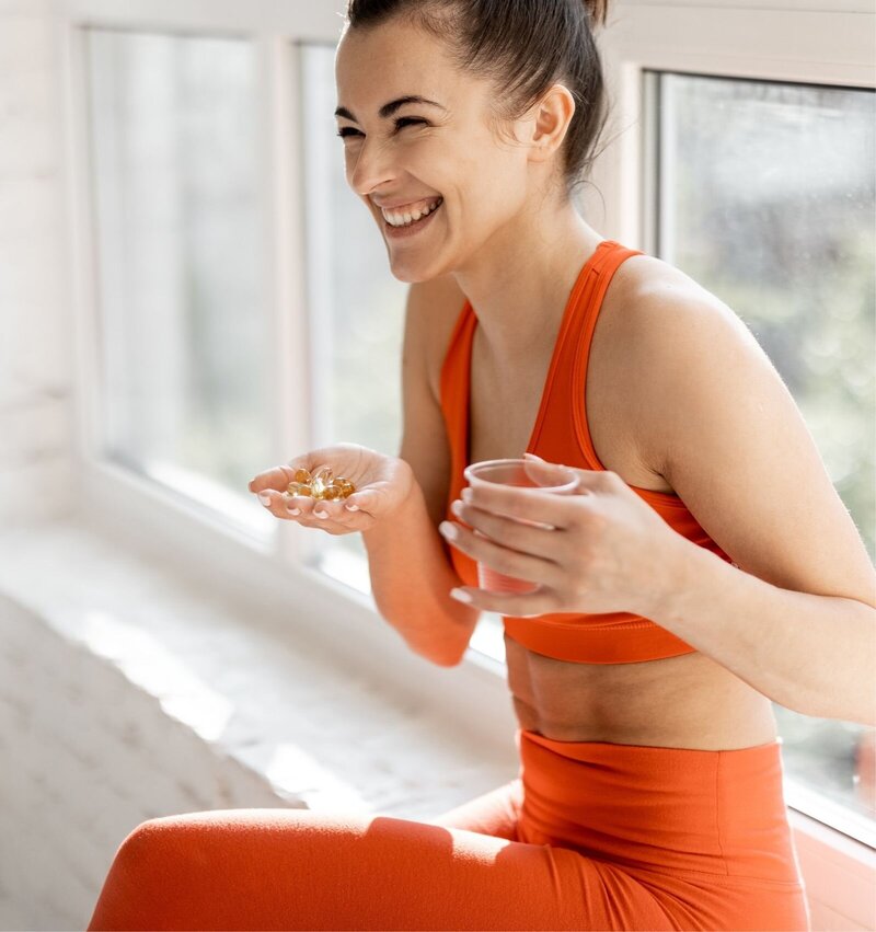 Woman smiling with supplements and water, representing tailored nutrition, supplement and lifestyle support with The Health Edits