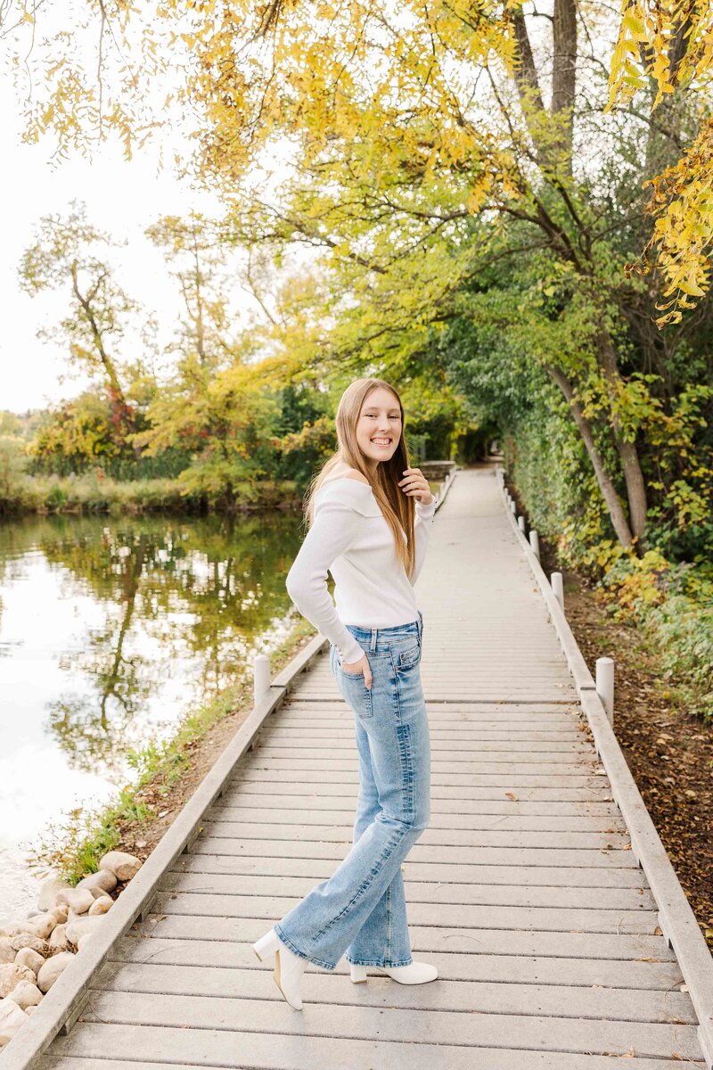Delafield Fish Hatchery Senior Fall Photoshoot.  Senior standing on a bridge with water reflection and color changing leaves in the Fall.