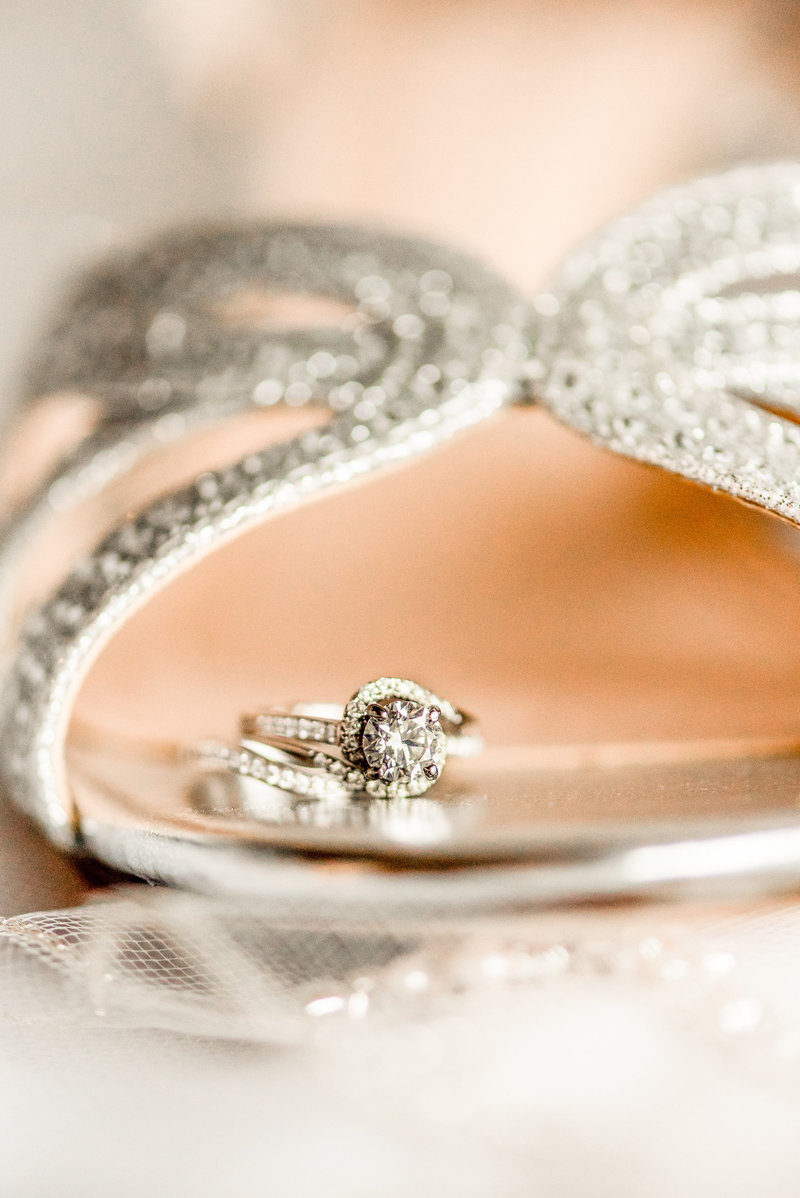 Diamond rings rest on the toe of a bride's shoe.