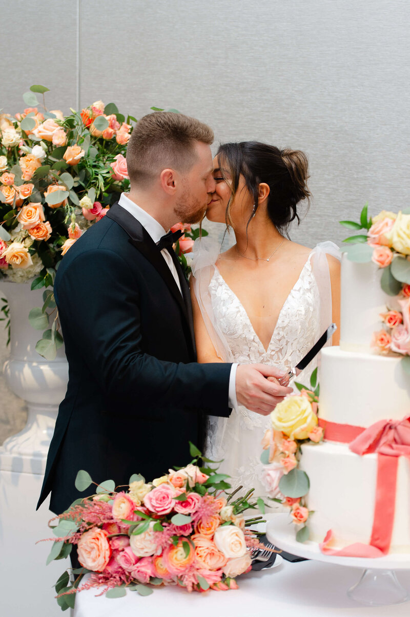 a bride and groom kiss while they cut their cake at their Chateau Le Parc wedding.  Captured by Ottawa wedding photographer JEMMAN Photography