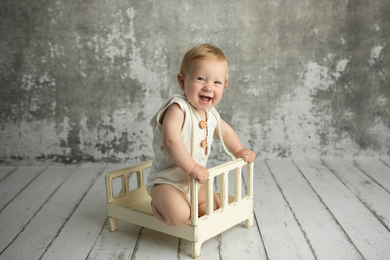 1 year old baby posing for milestone portraits with wooden backdrop