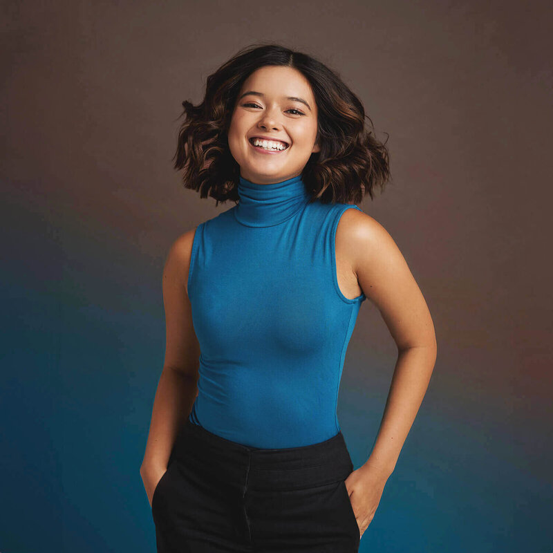 Vibrant photo of a woman in a  blue halter neck.  She's radiant and against a brown background with a blue gradient.