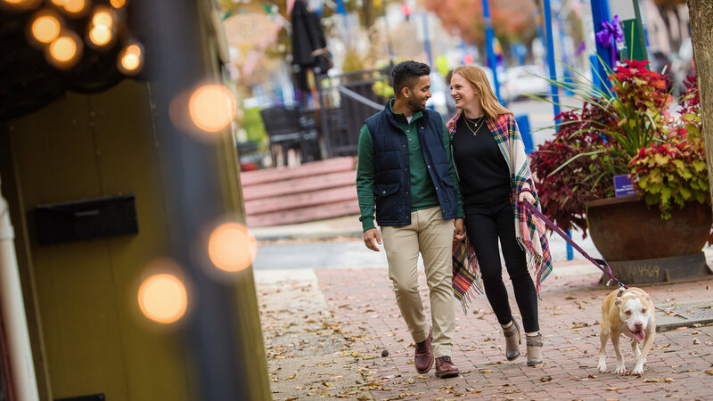 Engaged couple walking hand-in-hand with their dog along Bridge Street in Phoenixville during their engagement session.