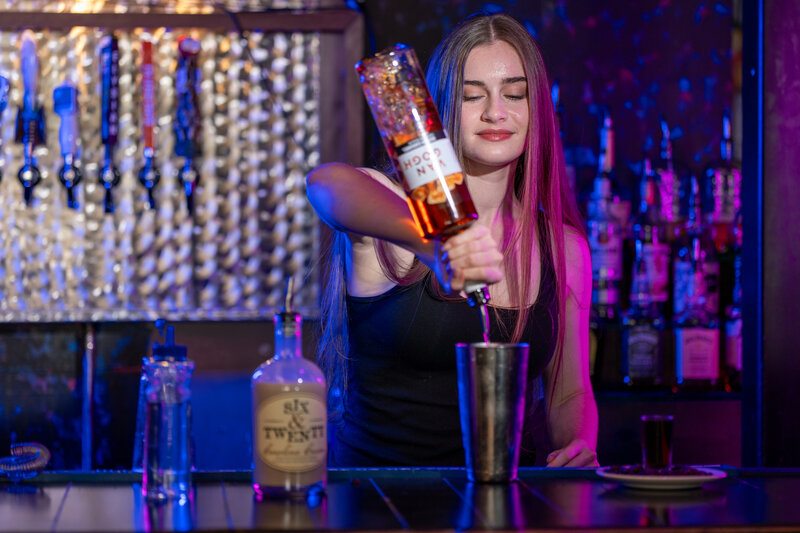 A bartender pouring alcohol into a mixer 