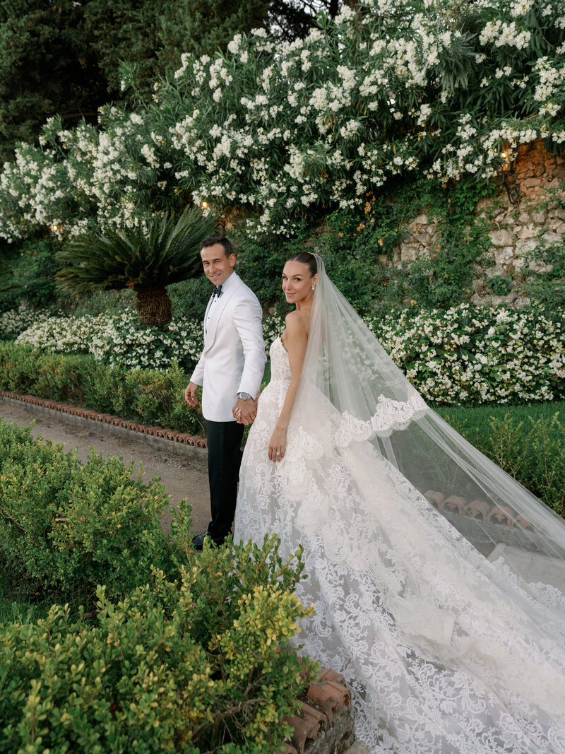 Bride in Monique Lhuillier walks with her groom in a garden after their wedding in Italy