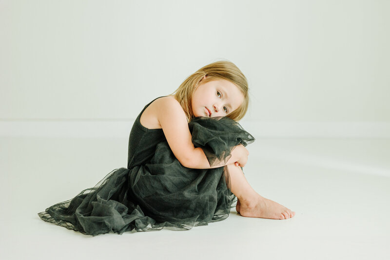 Little girl sitting on the floor in the studio wearing a black dress